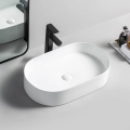 Biała owalna umywalka ceramiczna VICTORIA 46 Veldman z czarną baterią na jasnym blacie przed lustrem, widok z góry
