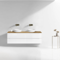 Szafka umywalkowa wisząca LINDA Veldman w kolorze białym, z blatem w kolorze dąb. z białymi umywalkami oraz ze złotymi bateriami ściennymi na tle jasnej ściany