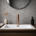 Nowoczesna łazienka z umywalką na drewnianej szafce z miedzianą baterią COSTA Veldman, betonową ścianą, cegłą w tle, lustrem oraz dekoracyjnym wazonem z kłosami.