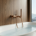 Bateria wannowa Costa w kolorze miedzi szczotkowanej z prysznicem ręcznym nad białą wanną przy drewnianej ścianie, z widokiem na góry.