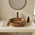 Umywalka nablatowa Anna w kolorze imitacji drewna z czarną baterią, okrągłym lustrem, ręcznikiem i dozownikiem na jasnym blacie.