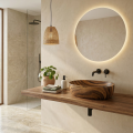 Minimalistyczna łazienka z drewnianą umywalką ANNA Veldman, okrągłym podświetlanym lustrem, półką z drewna, rośliną i lampą wiszącą.
