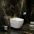 Podwieszany bidet Vito biały ze złotą krawędzią na tle czarnego marmuru ze złotymi żyłkami, z uchwytem na papier i szczotką WC.