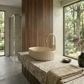 Nowoczesna łazienka z owalną umywalką Verona w kolorze beż mat na blacie terrazzo, złotą baterią i widokiem na las przez duże okna.