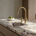 Nowoczesna kuchnia z marmurowym blatem, stalowym zlewem i złotą szczotkowaną baterią SIMONA Veldman zamontowaną na jasnej szafce, minimalistyczny styl.