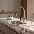 Nowoczesna kuchnia z marmurowym blatem, stalowym zlewem i złotą szczotkowaną baterią SIMONA Veldman zamontowaną na jasnej szafce, minimalistyczny styl.