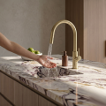 Nowoczesna kuchnia z marmurowym blatem, stalowym zlewem i złotą szczotkowaną baterią SIMONA Veldman zamontowaną na jasnej szafce, minimalistyczny styl.