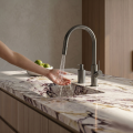 Dłoń odkręca wodę w stalowej baterii SIMONA nad marmurowym zlewem, obok miska z limonkami.