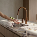 Dłoń odkręca wodę w stalowej baterii SIMONA nad marmurowym zlewem, obok miska z limonkami.