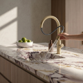 Nowoczesna kuchnia z marmurowym blatem, stalowym zlewem i złotą szczotkowaną baterią SIMONA - z wyciągniętą wylewką - zamontowaną na jasnej szafce, minimalistyczny styl.