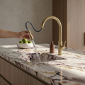 Nowoczesna kuchnia z marmurowym blatem, stalowym zlewem i złotą szczotkowaną baterią SIMONA - z wyciągniętą wylewką - zamontowaną na jasnej szafce, minimalistyczny styl.
